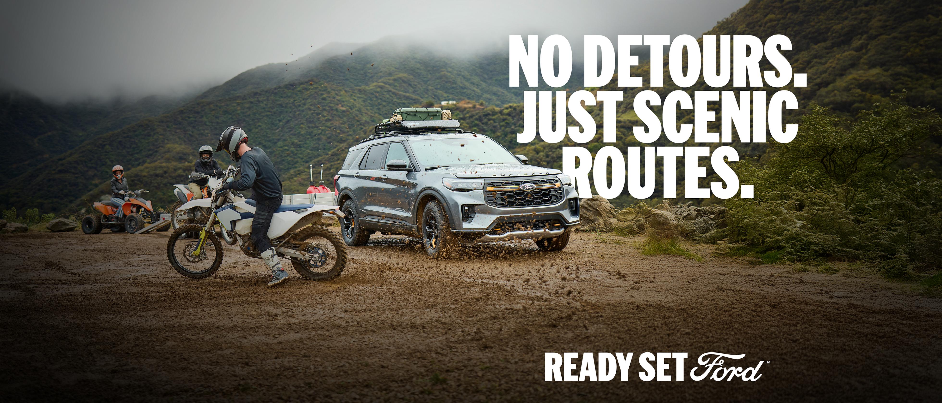 A 2026 Ford Explorer® Tremor® SUV with a trailer parked at a mountain overlook with a person riding a dirtbike nearby