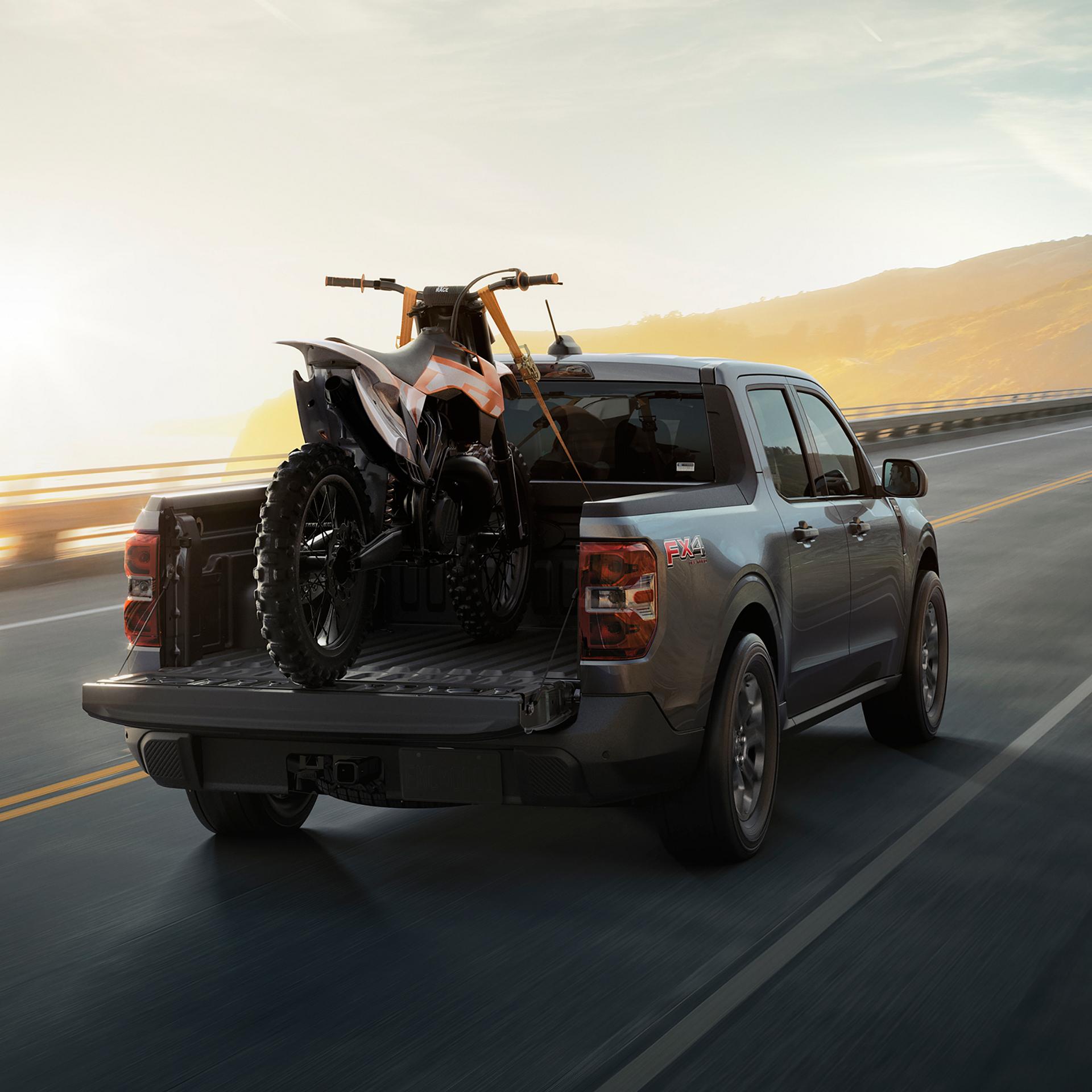 2026 Ford Maverick® Tremor® model with a motorcycle strapped in the bed being driven on the highway