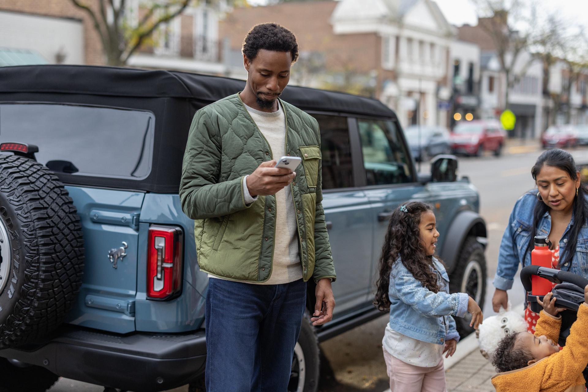 A man looks at his phone while standing beside his Ford Bronco®