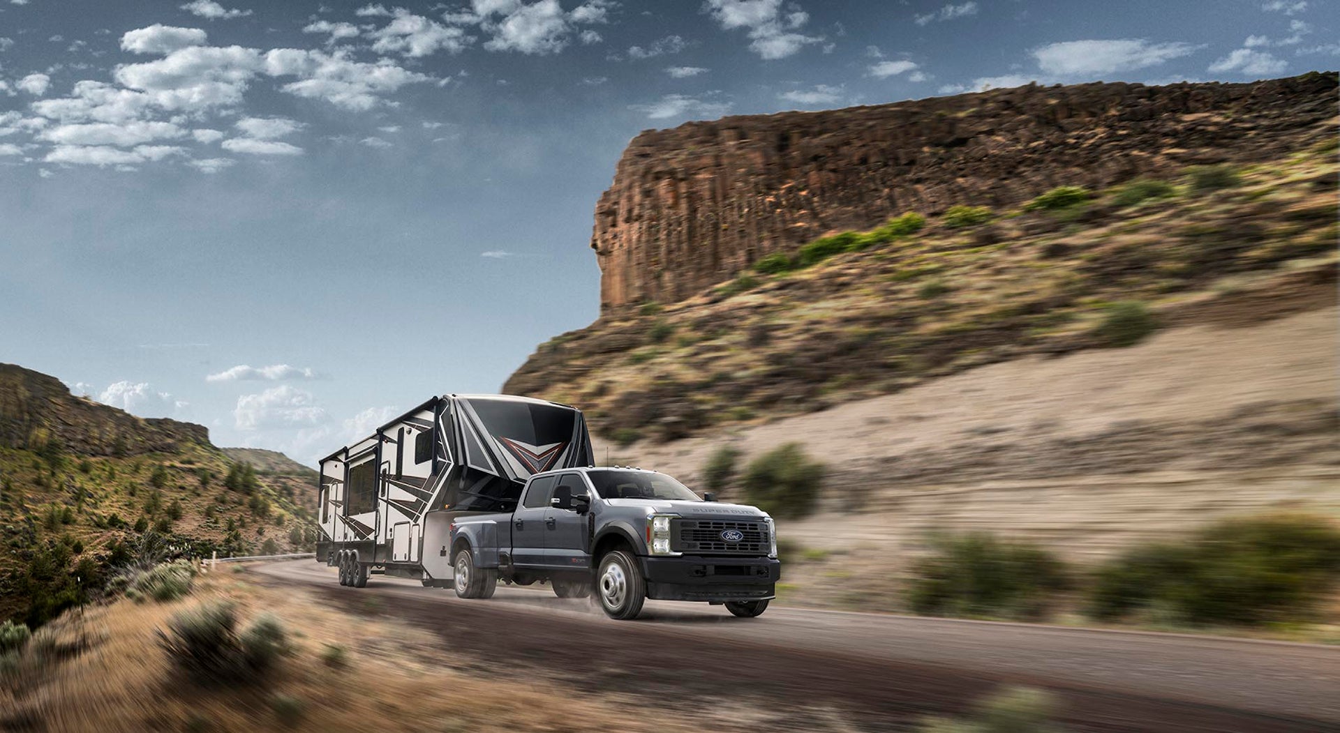 Gray Ford Super Duty F-450 XL towing a fifth-wheel camper on a desert road