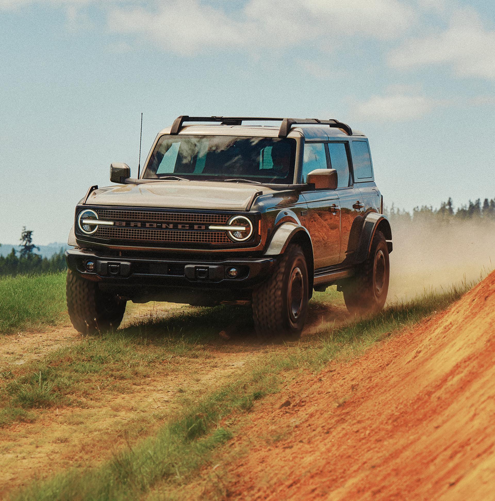 A 2027 Ford Bronco® Filson™ SUV being driven on a dirt trail near a hillside