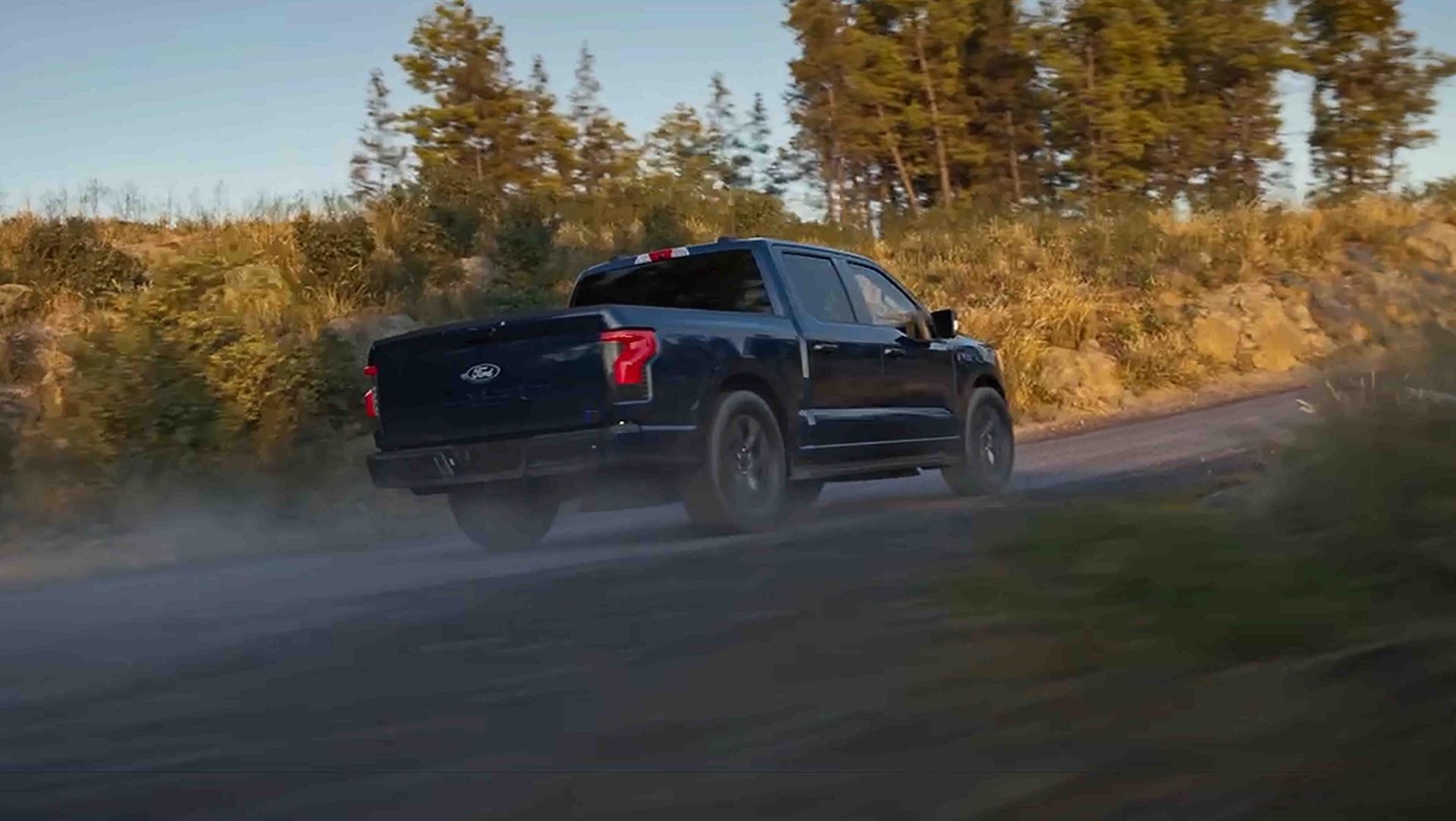 A black 2025 Ford F-150® Lightning® pickup driving on a gravel road kicking up dust
