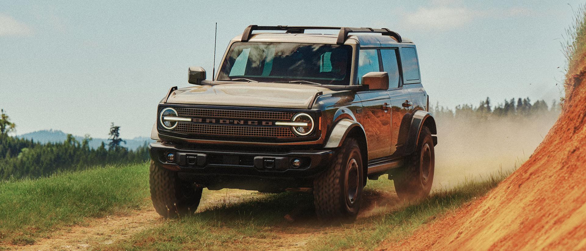 A 2027 Ford Bronco® Filson™ SUV being driven on a dirt trail near a hillside