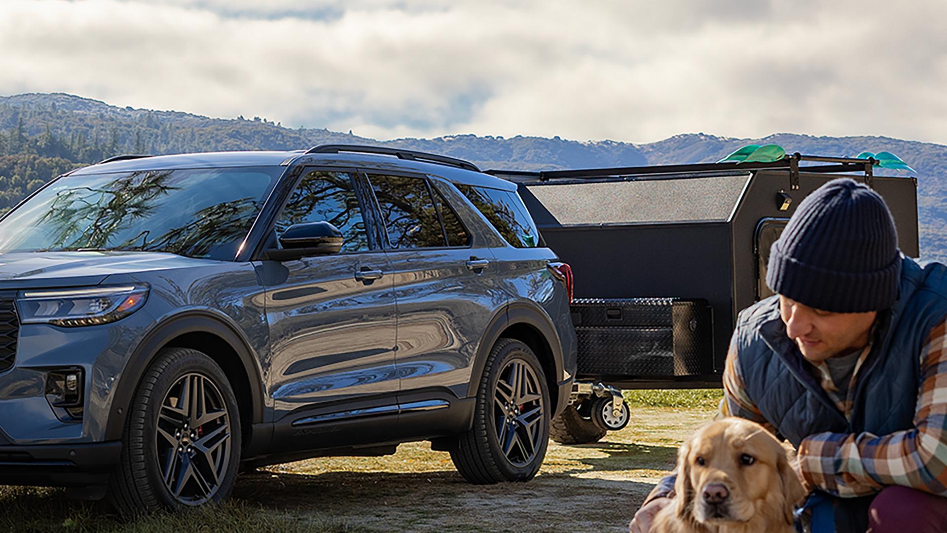 A 2026 Ford Explorer® parked outside towing a camper with a man and dog in the foreground
