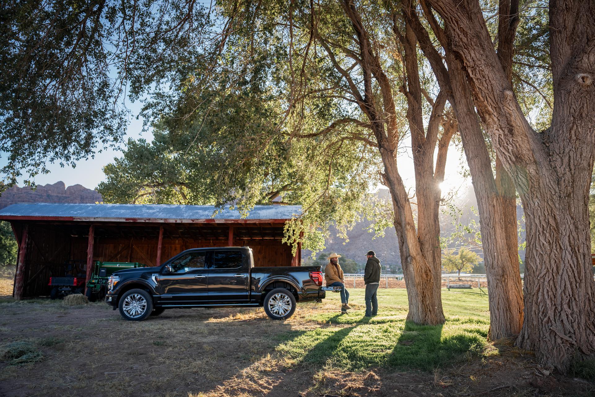 Ford F-150® parked on a farm with a cowboy sitting on the tailgate talking to a man