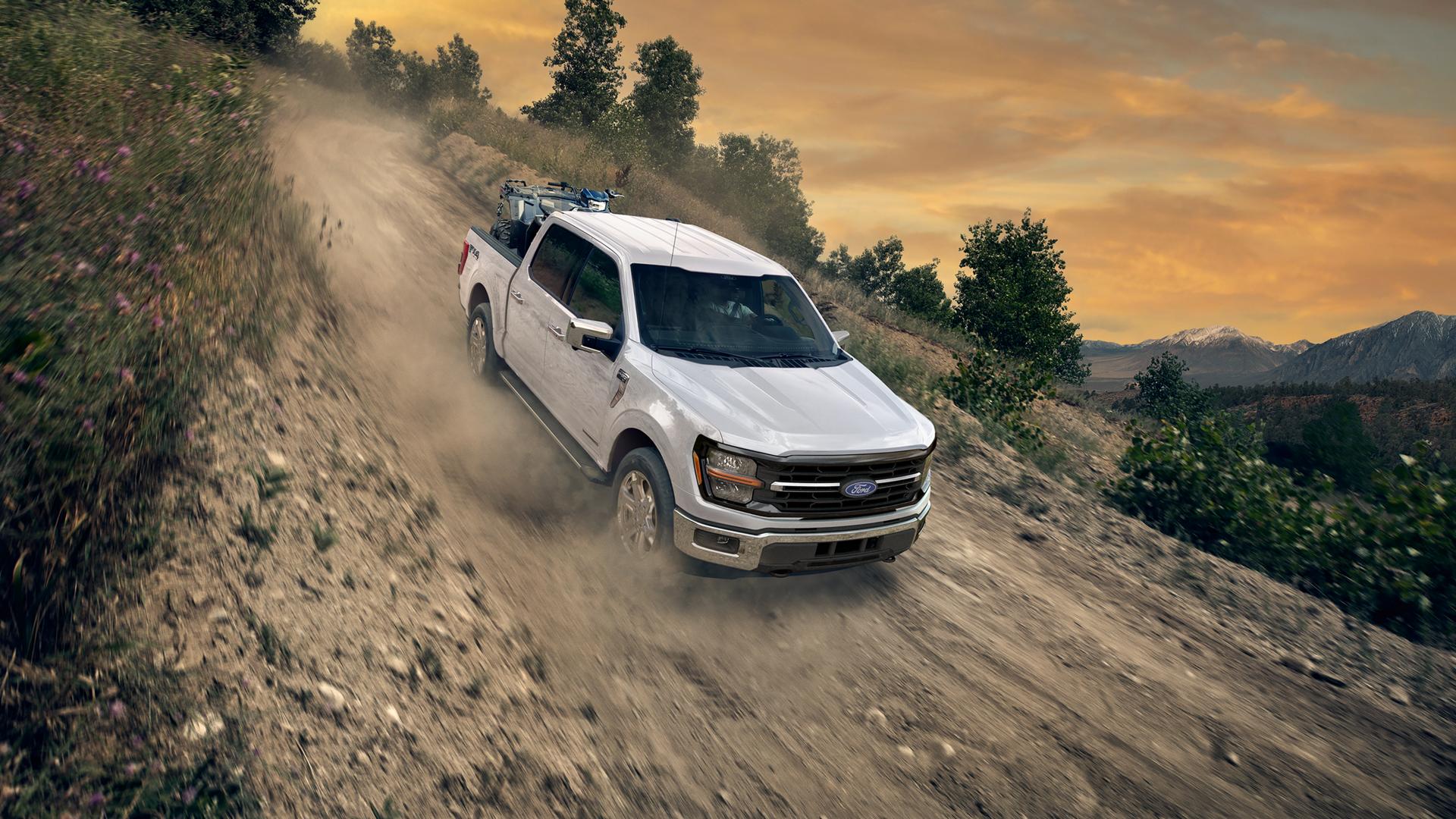 2026 Ford F-150® STX® FX4 pickup in Oxford White being driven down a dirt road with an ATV in the bed