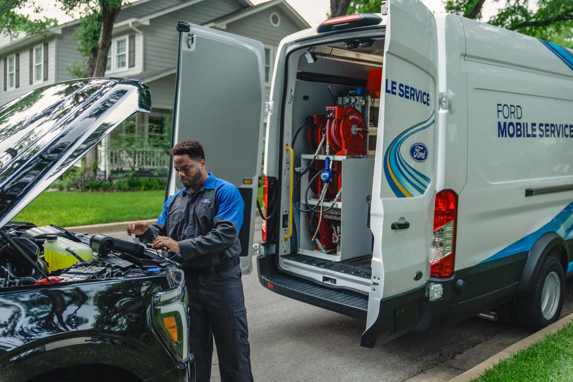A Ford Mobile Service tech works under the hood of a Ford truck with the open doors of the Mobile Service van behind them