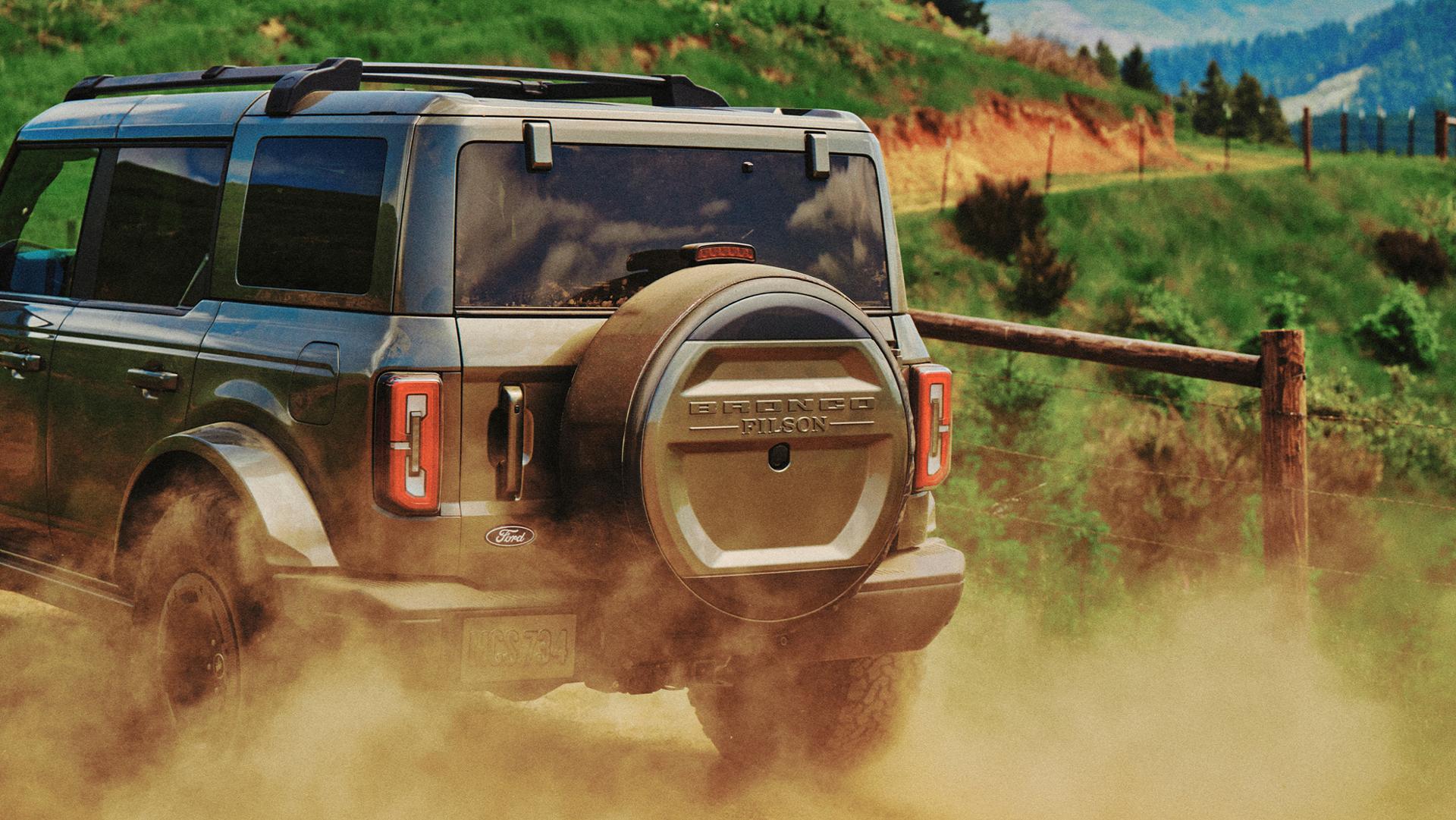 A view from behind a 2027 Ford Bronco® Filson SUV as it kicks up dust on a dirt trail