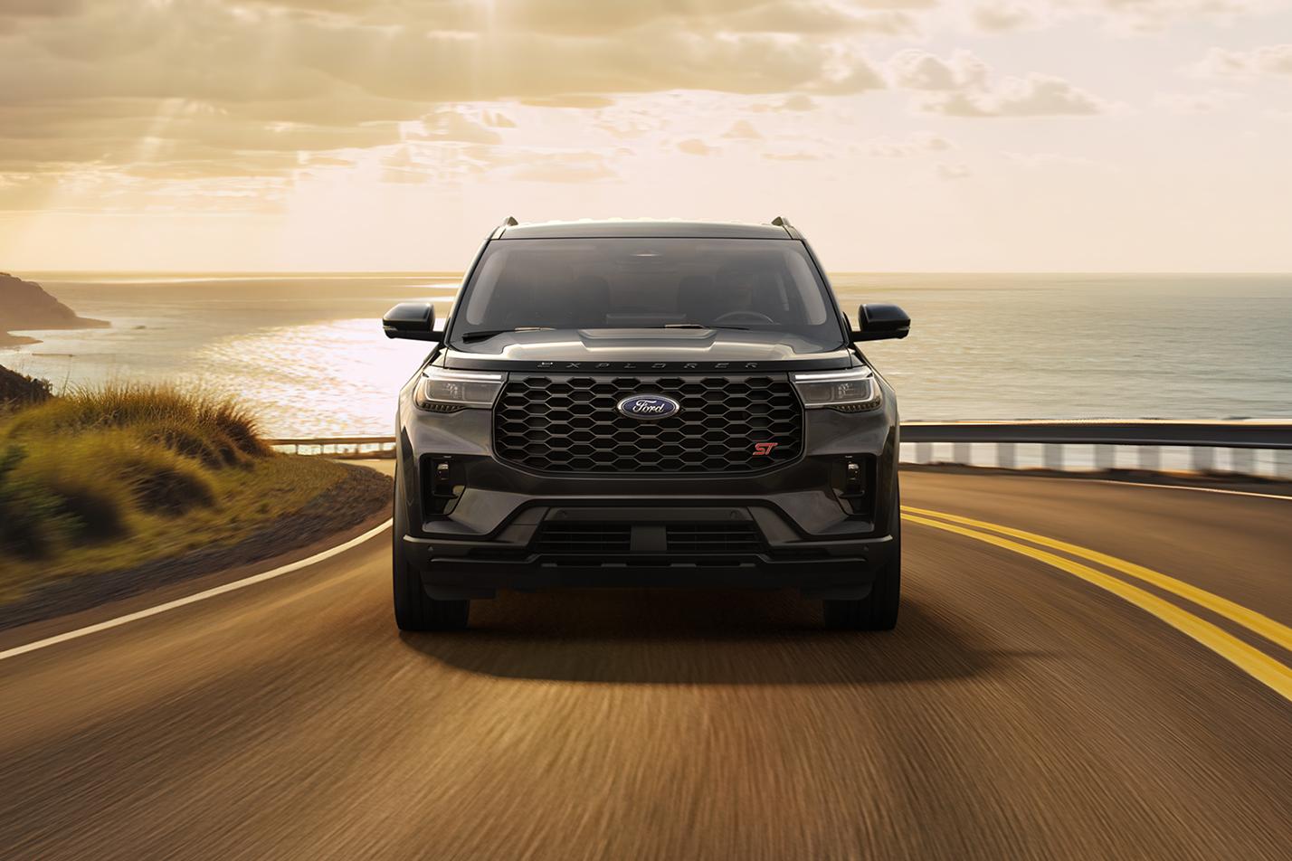 A Ford Explorer® SUV is driven along a winding coastal highway as the sun breaks through clouds behind it