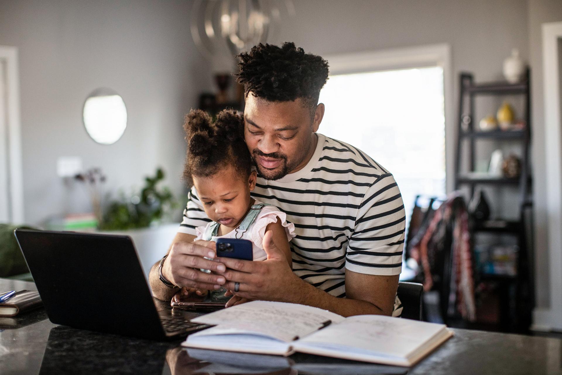 A man holds his child in his lap while interacting with the Ford app on his phone