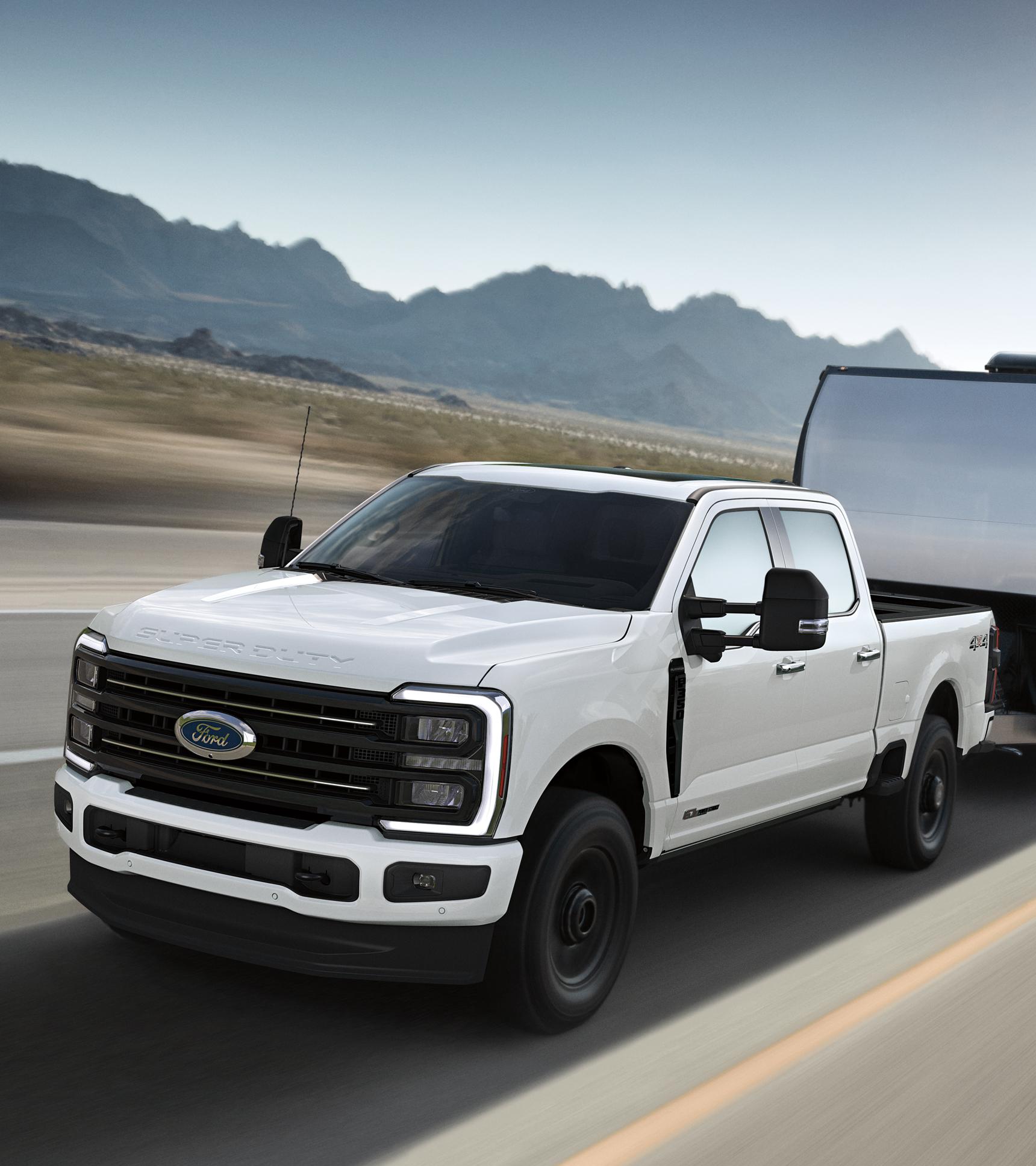 A 2026 Ford Super Duty® F-350® Platinum® model in Star White pulling a large trailer on a paved road