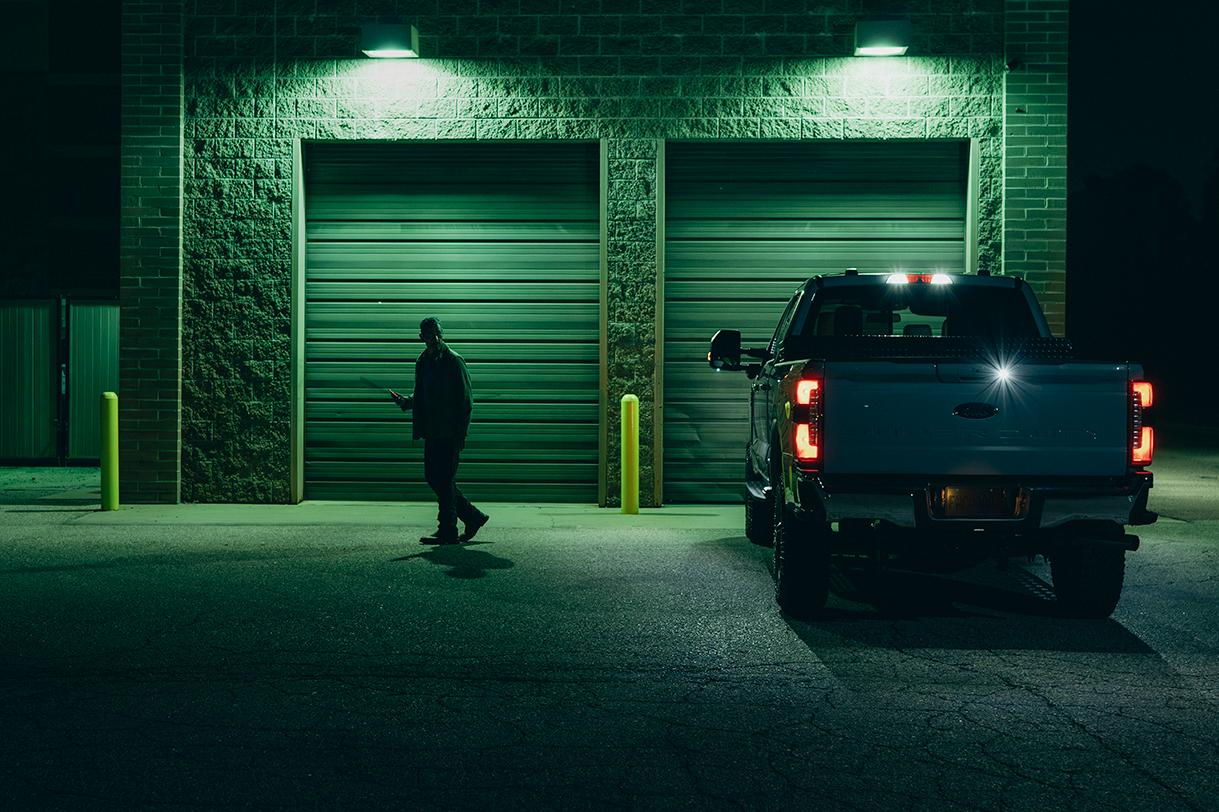 A Ford F-150® parked in front of a garage at night while a man walks away