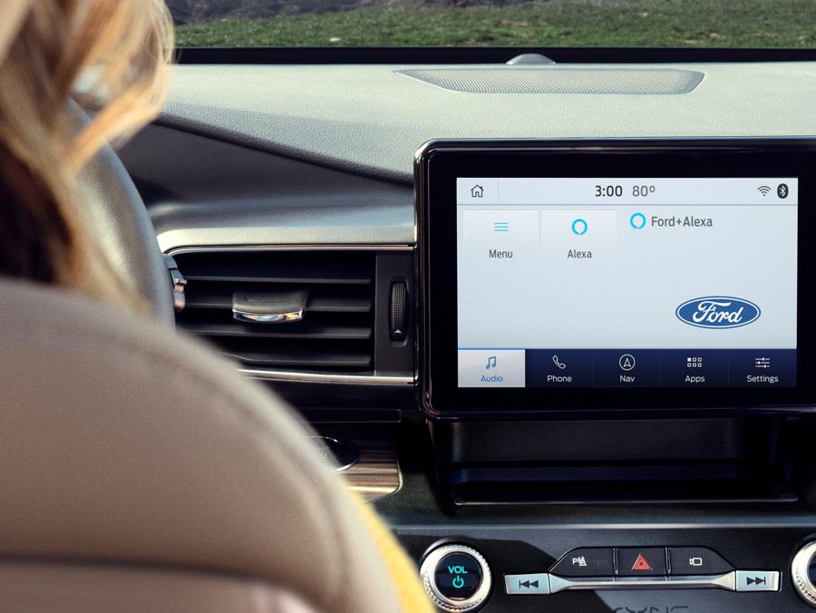 A view from the backseat of a parked Ford vehicle, looking toward the SYNC touchscreen atop the center stack. The screen is displaying a menu for choosing a music source.