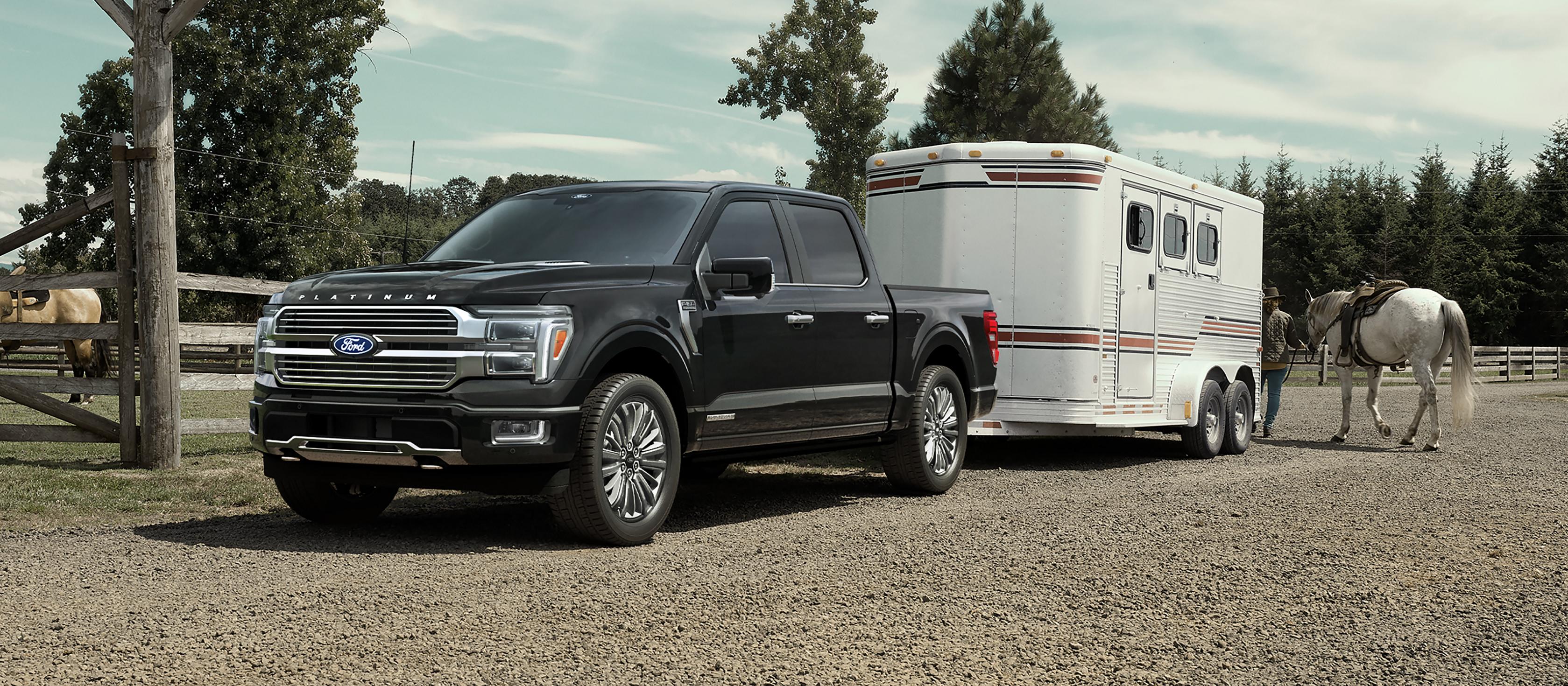 2026 Ford F-150® Platinum® pickup in Agate Black hitched to a horse trailer parked near a ranch