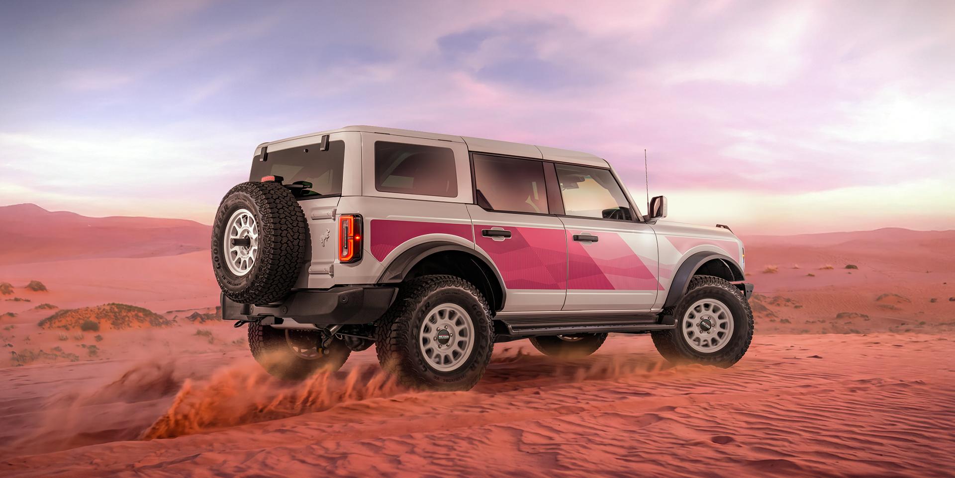 Rear three-quarter view of the Bronco climbing a desert dune at sunset
