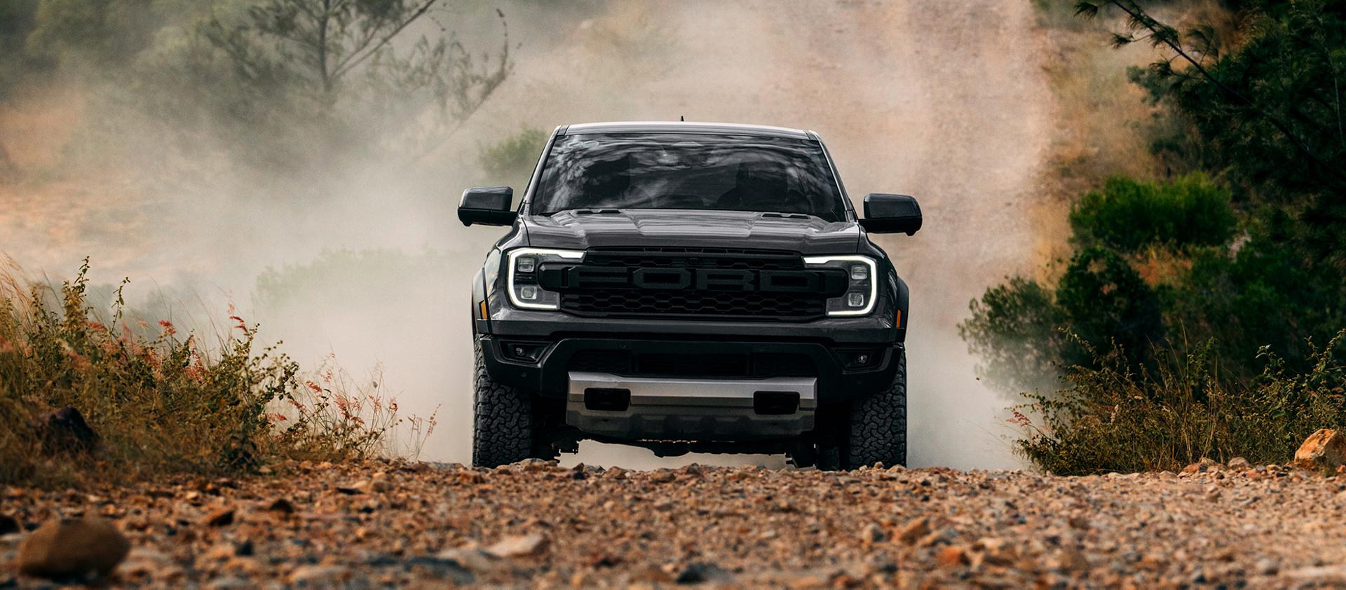 A dark 2026 Ford Ranger® Raptor® driving head-on down a dirt trail, kicking up dust