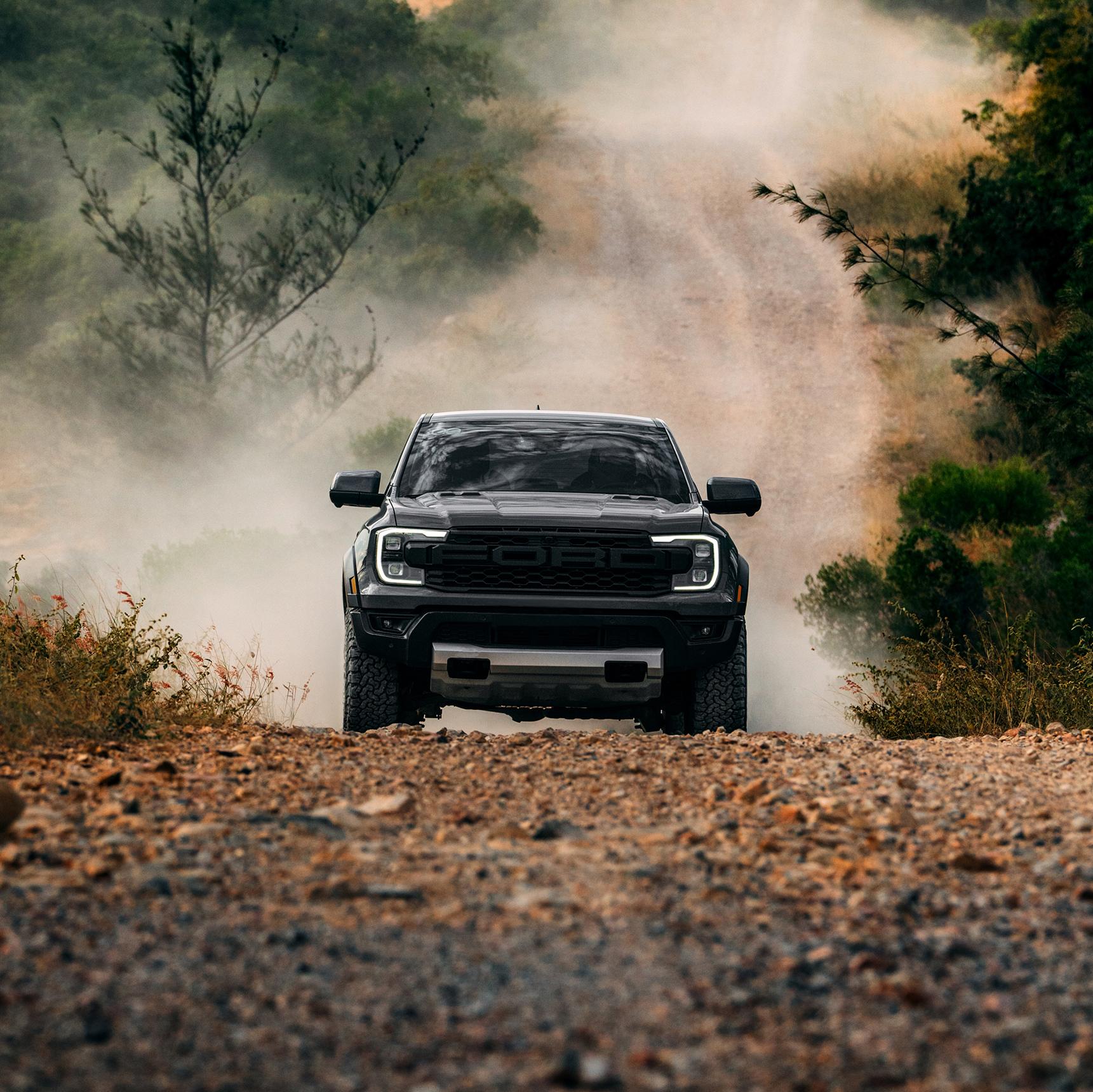 A dark 2026 Ford Ranger® Raptor® driving head-on down a dirt trail, kicking up dust