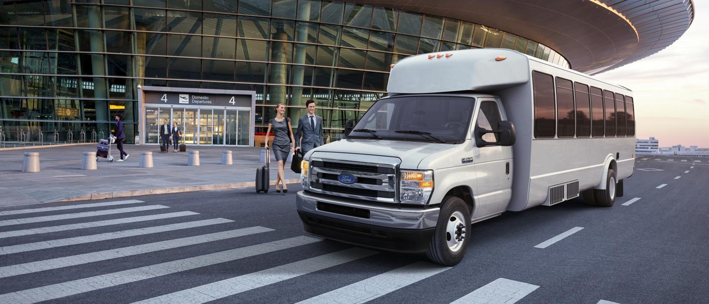 2026 Ford E-Series Cutaway with aftermarket shuttle bus body being driven near passengers