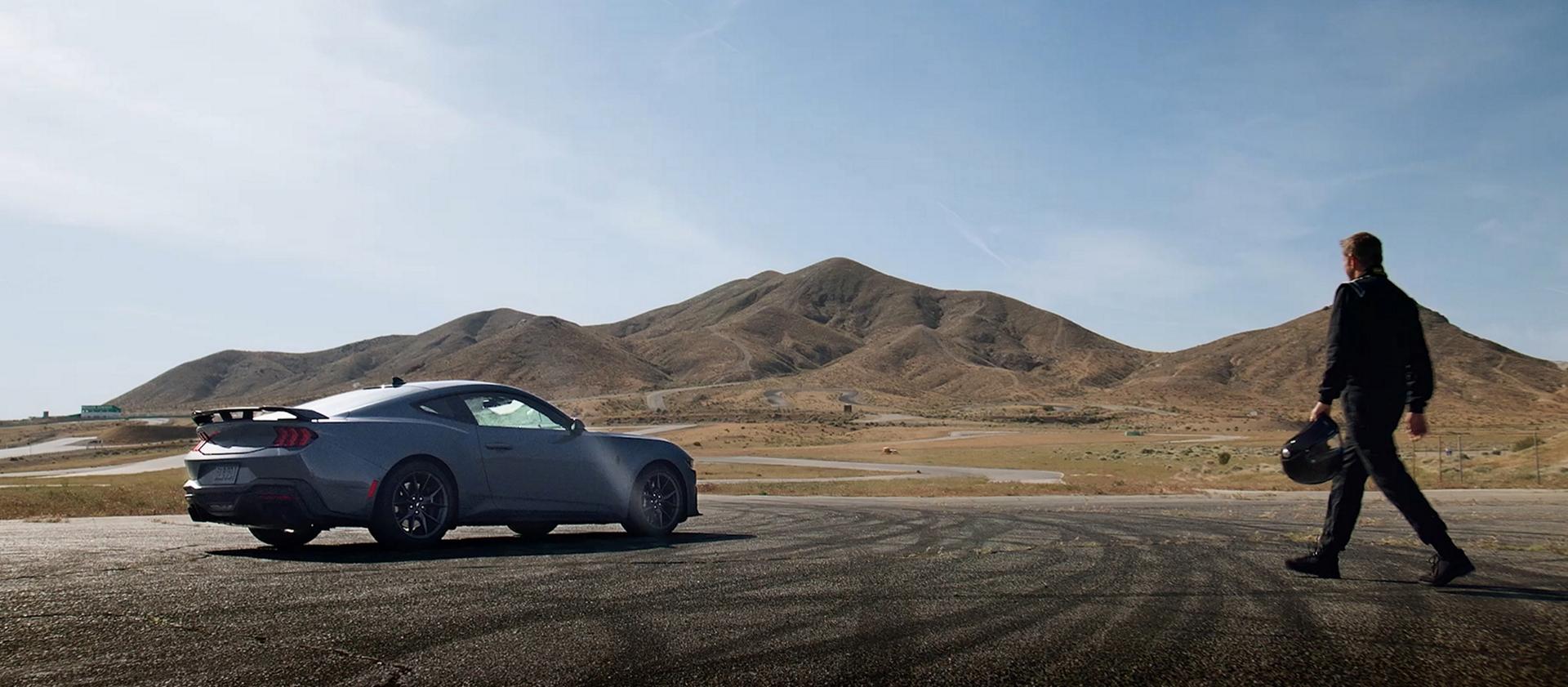 A person holding a racing helmet walking toward a Ford Mustang®