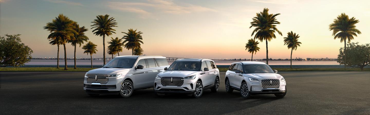 Three Lincoln SUVs parked side by side in front of palm trees at sunset.