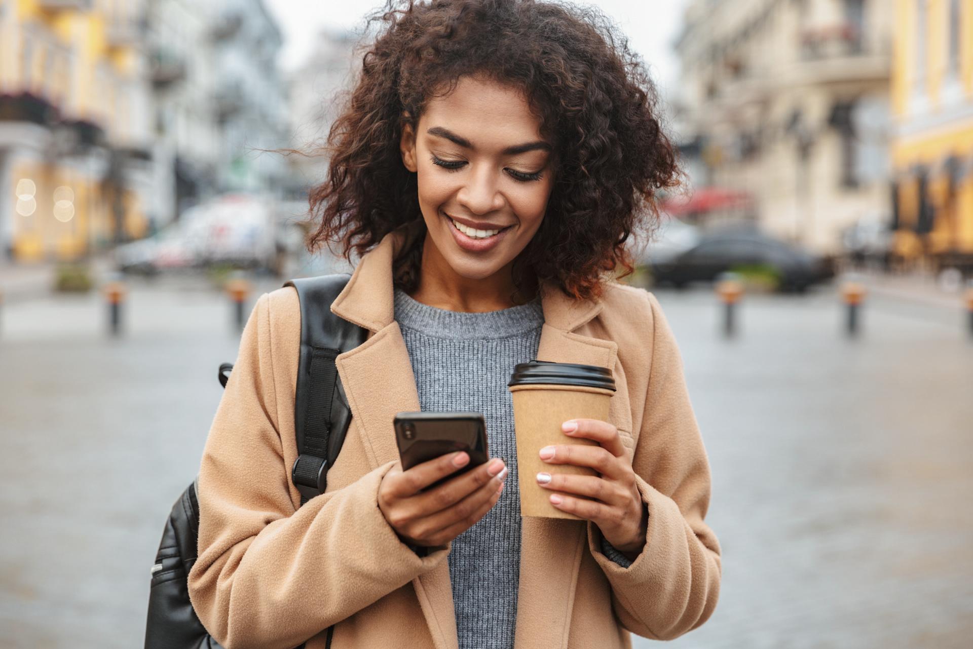 Woman holding a smartphone in one hand and a coffee cup in her other hand