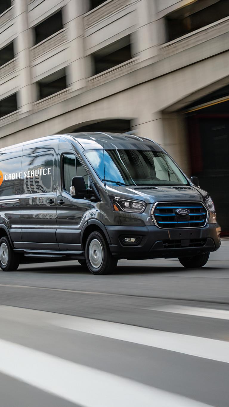 A gray 2026 Ford E-Transit™ van being driven down a city street