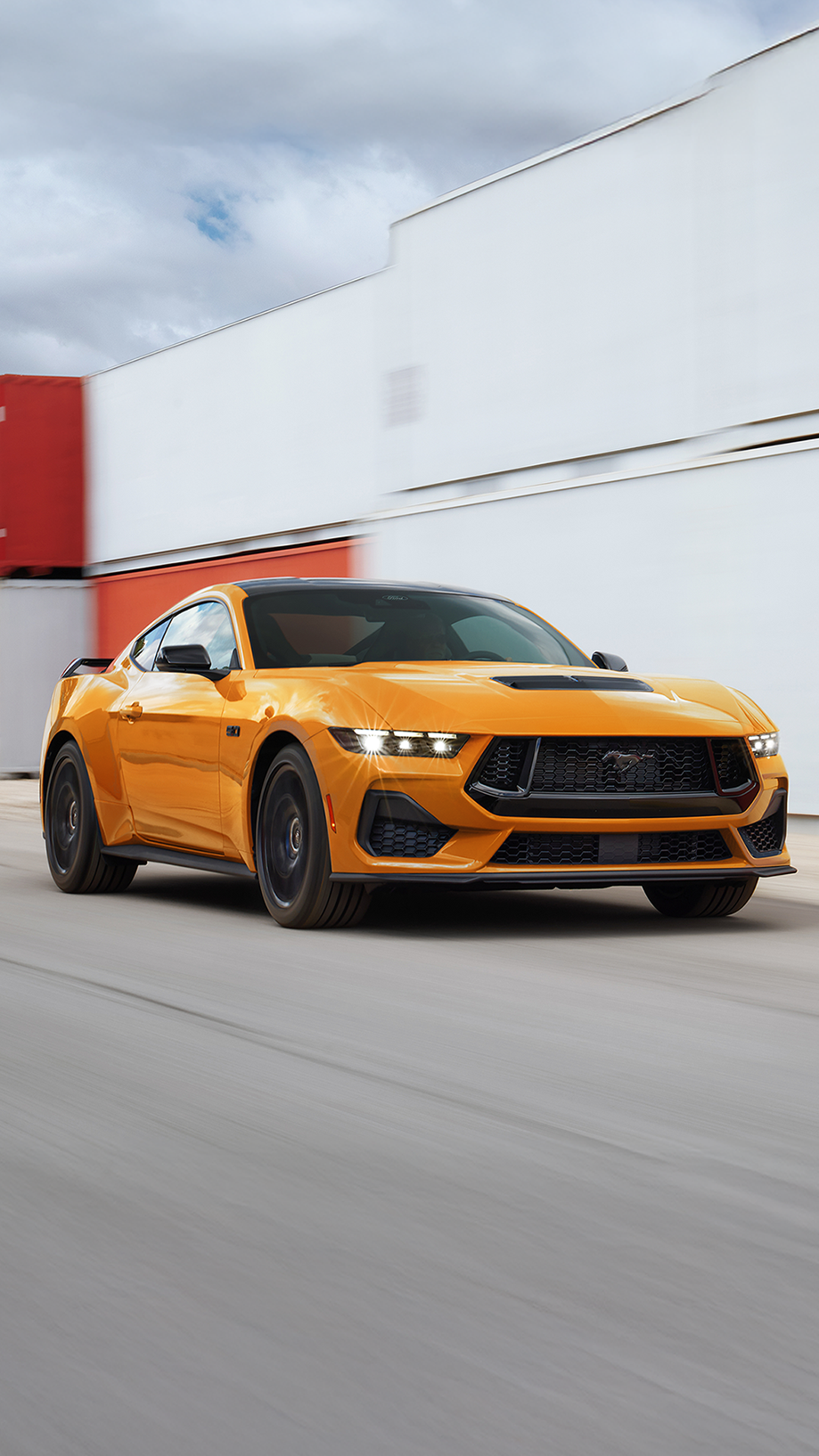 2026 Ford Mustang® GT fastback in Orange Fury Metallic Tri-coat being driven near shipping containers