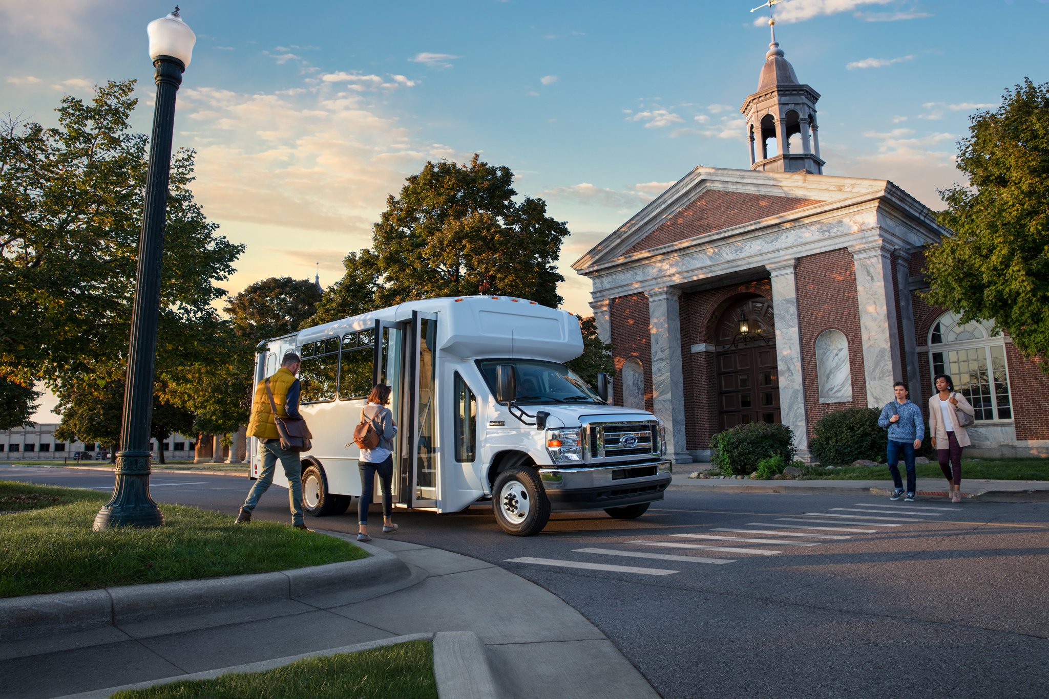Des personnes montent à bord d’un véhicule tronqué à roues arrière jumelées de la série E de 2025 de Ford avec modification pour bus-navette