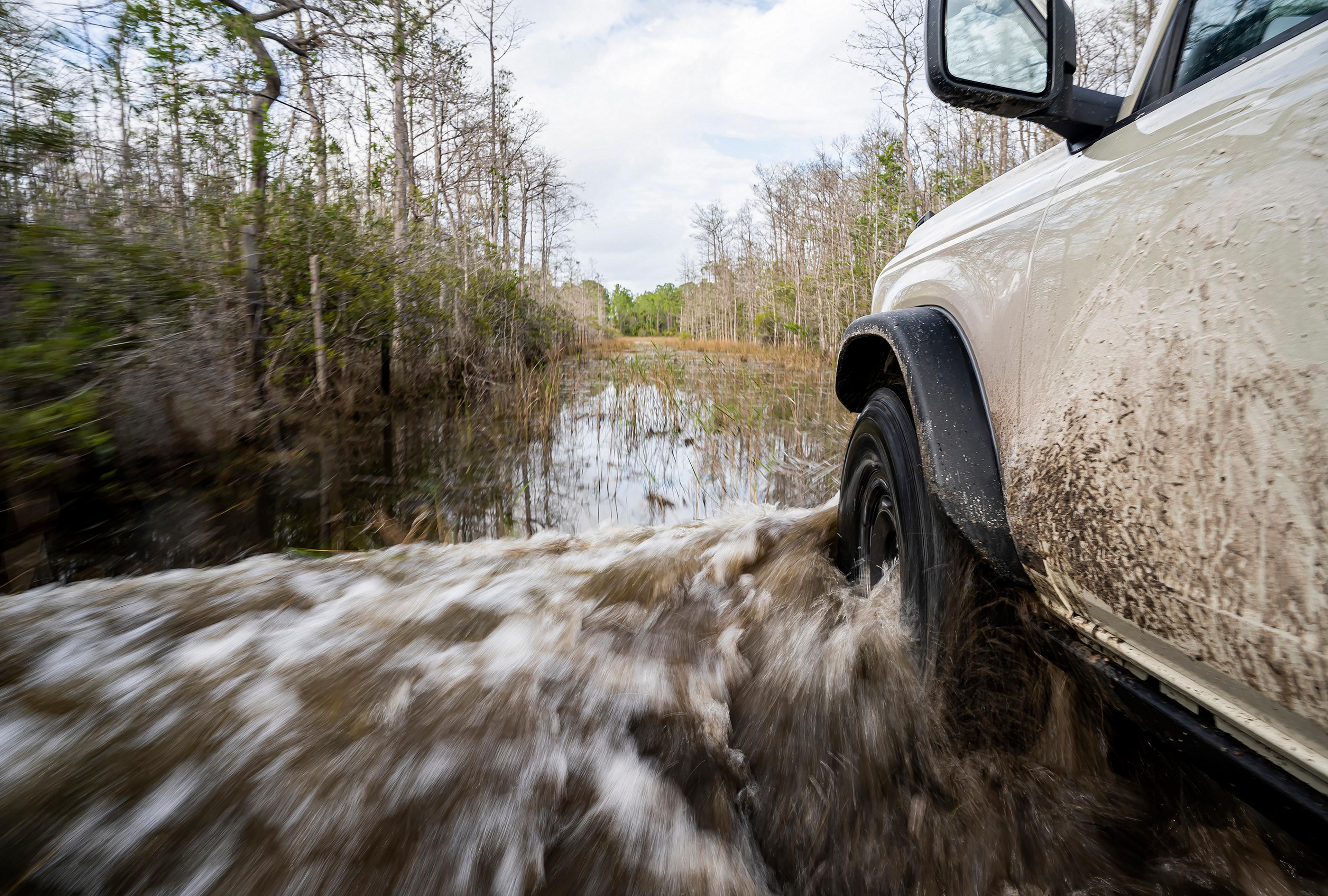 A close-up of the front driver's-side wheel and fender of a 2026 Ford Bronco® SUV as it's driven through a river