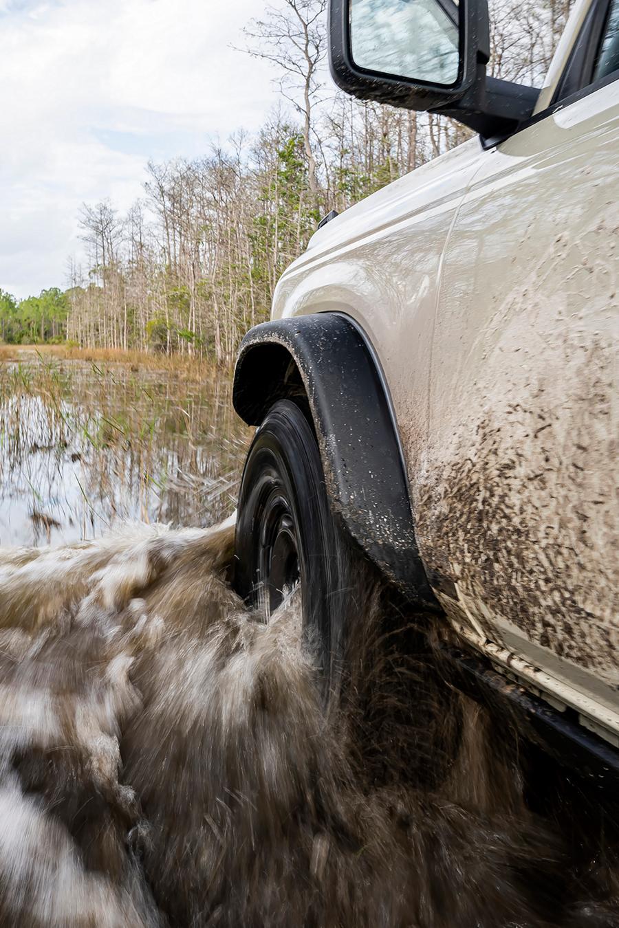 A close-up of the front driver's-side wheel and fender of a 2026 Ford Bronco® SUV as it's driven through a river