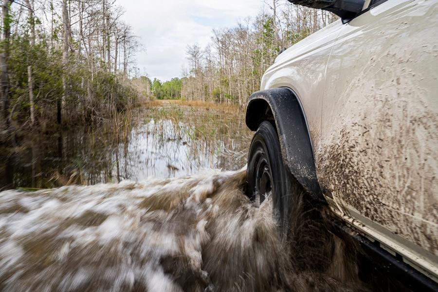 A close-up of the front driver's-side wheel and fender of a 2026 Ford Bronco® SUV as it's driven through a river