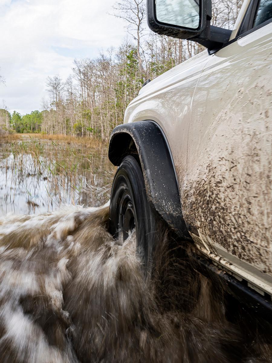 A close-up of the front driver's-side wheel and fender of a 2026 Ford Bronco® SUV as it's driven through a river