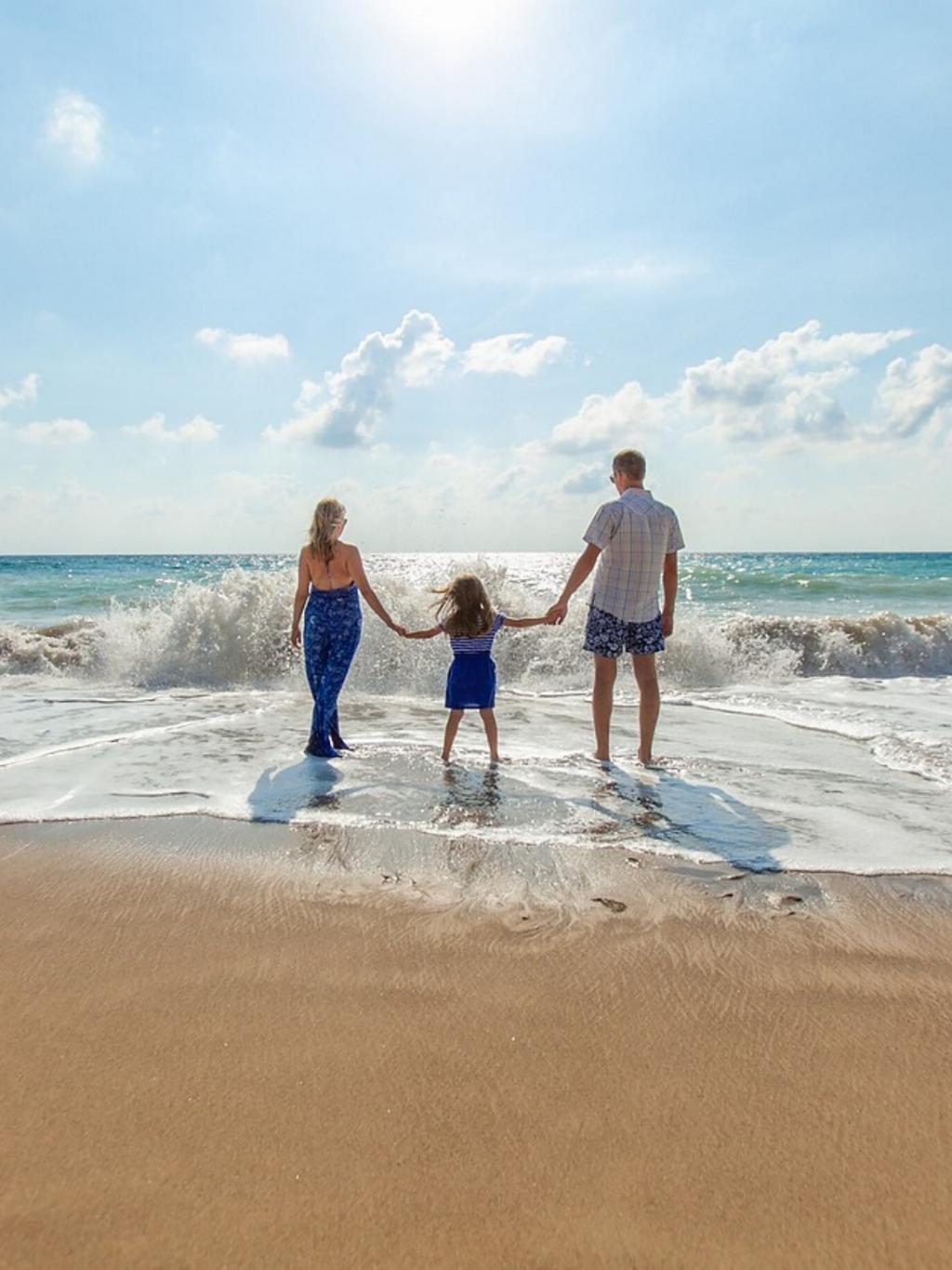 A family of three walk in the surf of an ocean