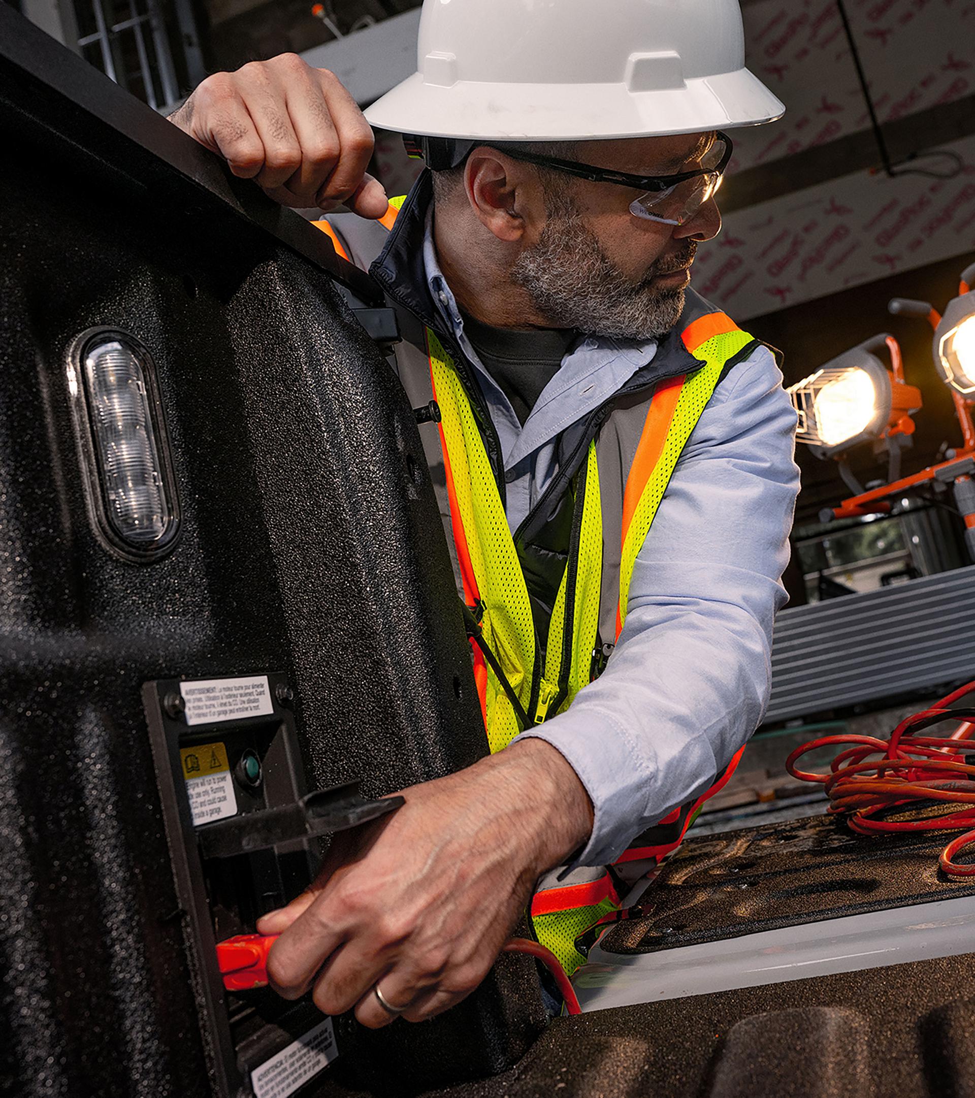 A male construction worker plugging into the Pro Power Onboard in a 2026 Ford Super Duty’s bed