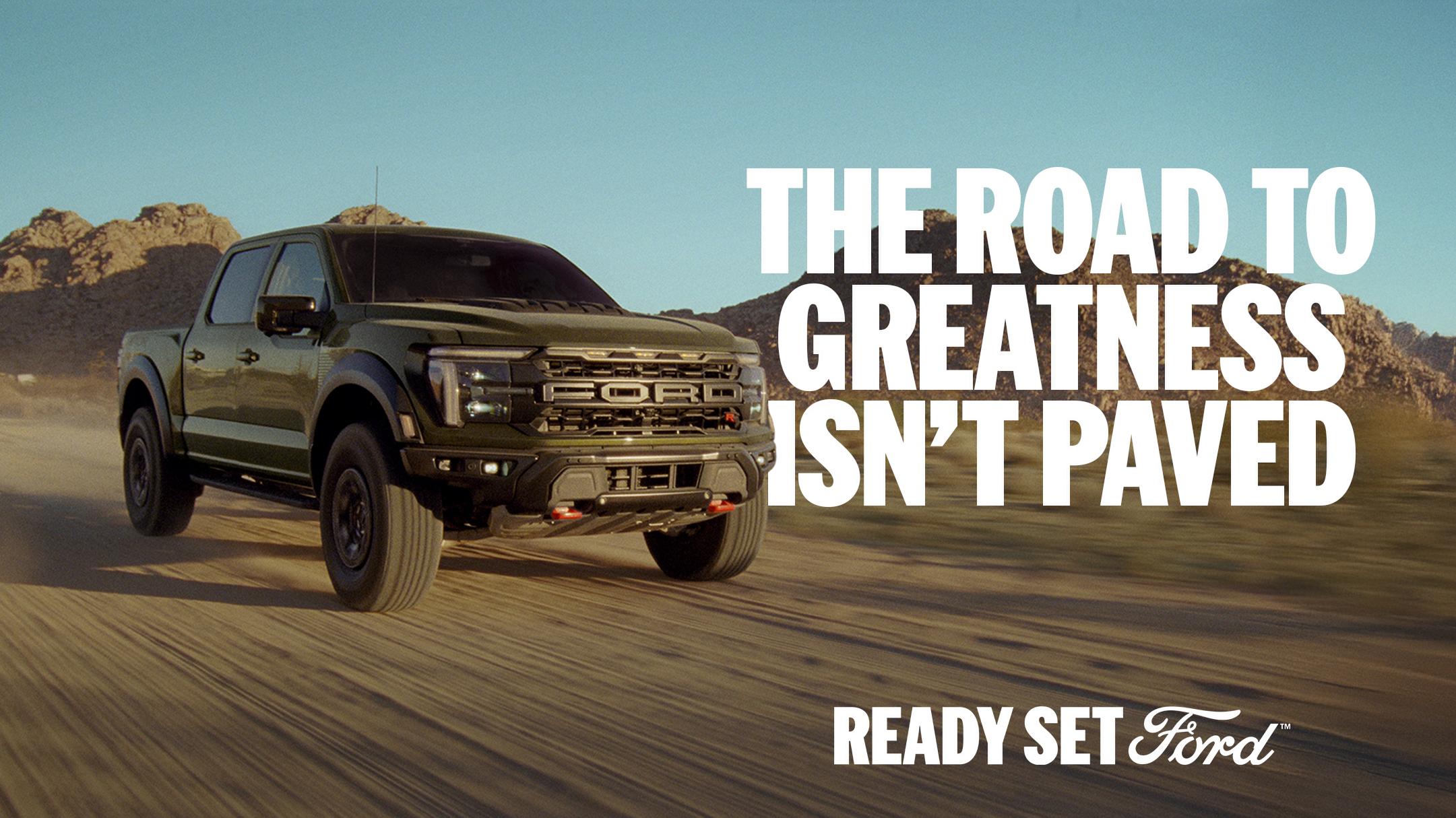 A Black 2026 Ford F-150® Raptor® R™ driving on a desert dirt road surrounded by mountains