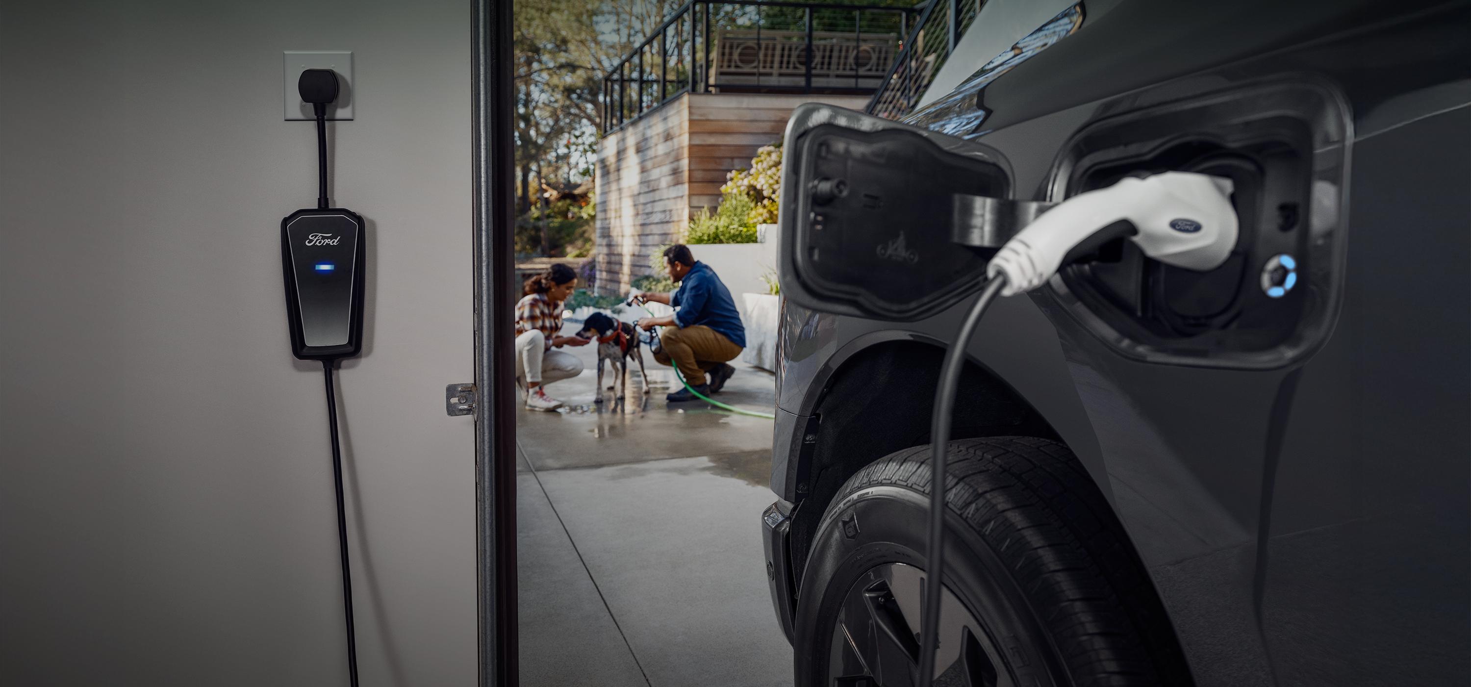 A 2025 Ford F-150® charges in the foreground as two people bathe their dog in the driveway