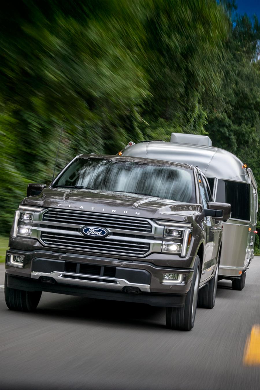 A 2025 Ford F-150® Platinum® Plus truck driving on the highway while towing a camper trailer