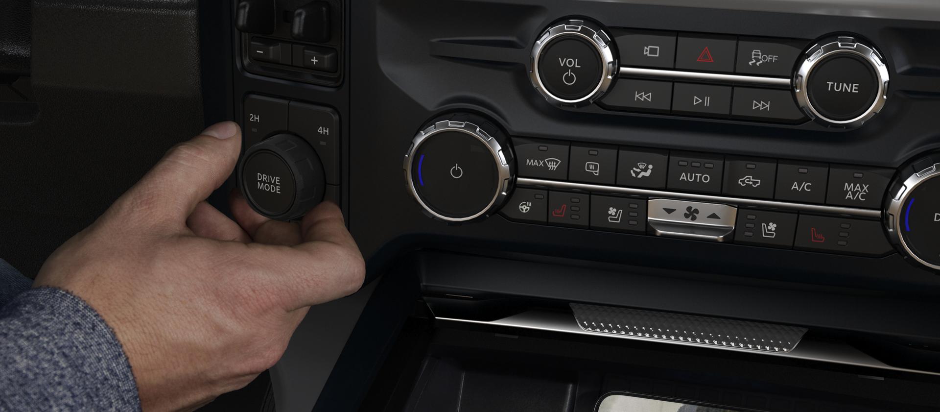 A person's hand adjusting the Drive Mode knob inside their 2026 Ford Super Duty® pickup, while their phone charges with the wireless charging pad