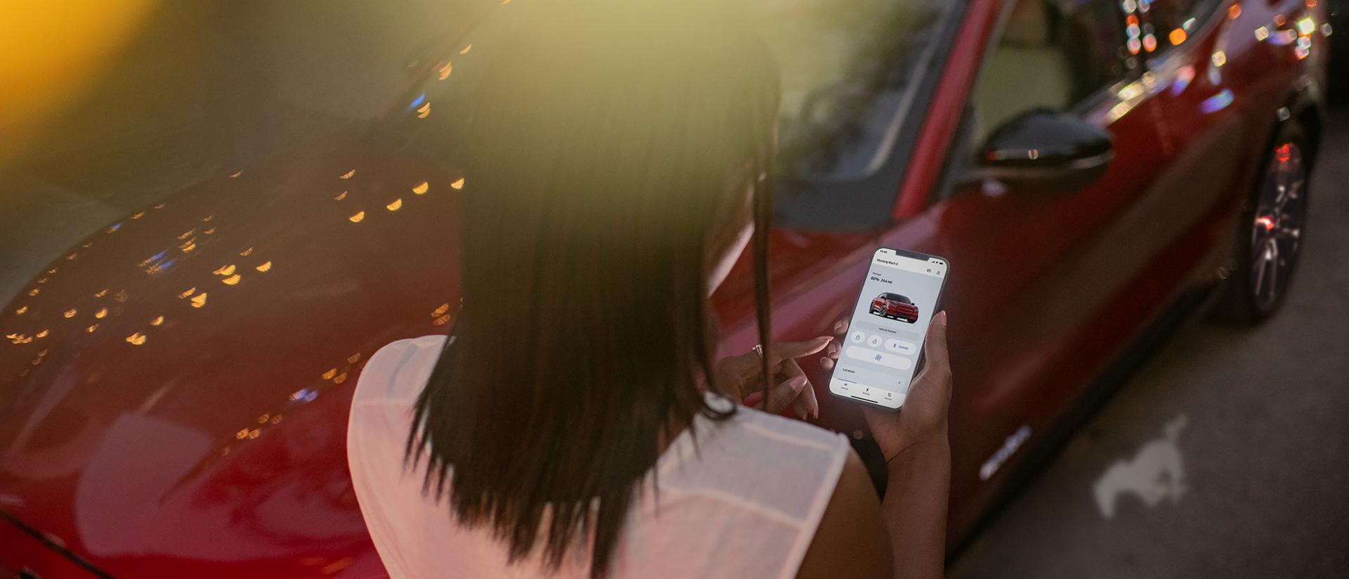 Woman standing next to a Ford Mustang Mach-E® looking at the FordPass® app on a phone