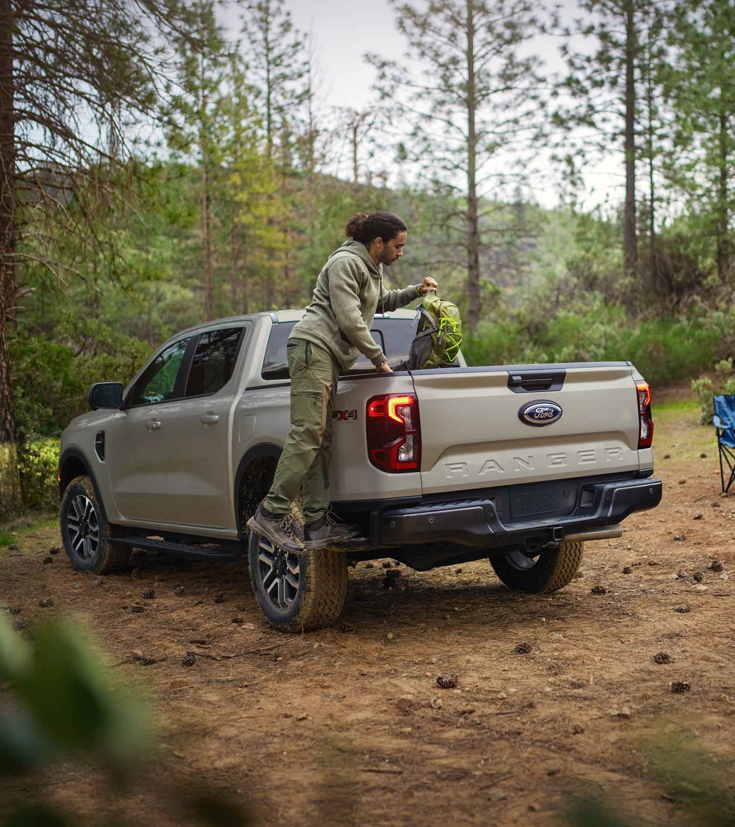 Person climbing into the bed of their 2026 Ford Ranger® Lariat® model with a back pack