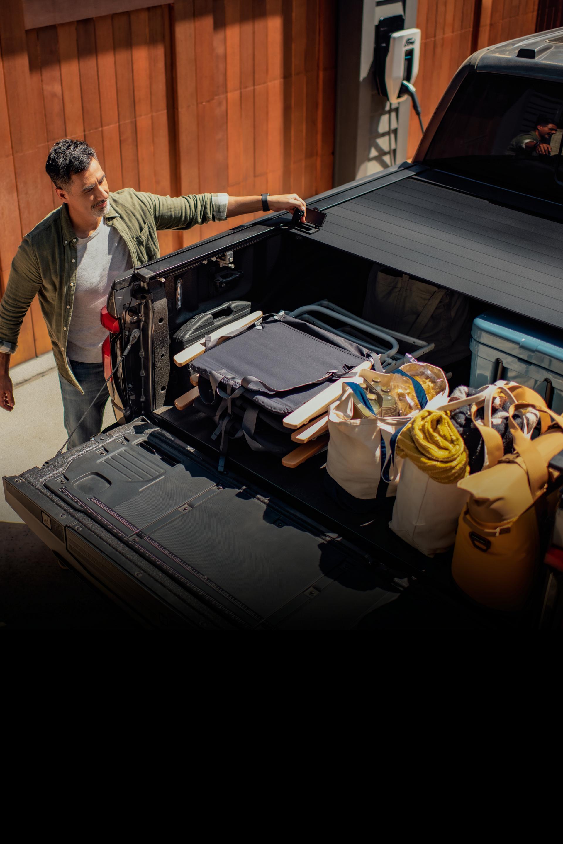 A 2025 Ford F-150® Lightning® truck parked as a man is closing a truck bed filled with bags