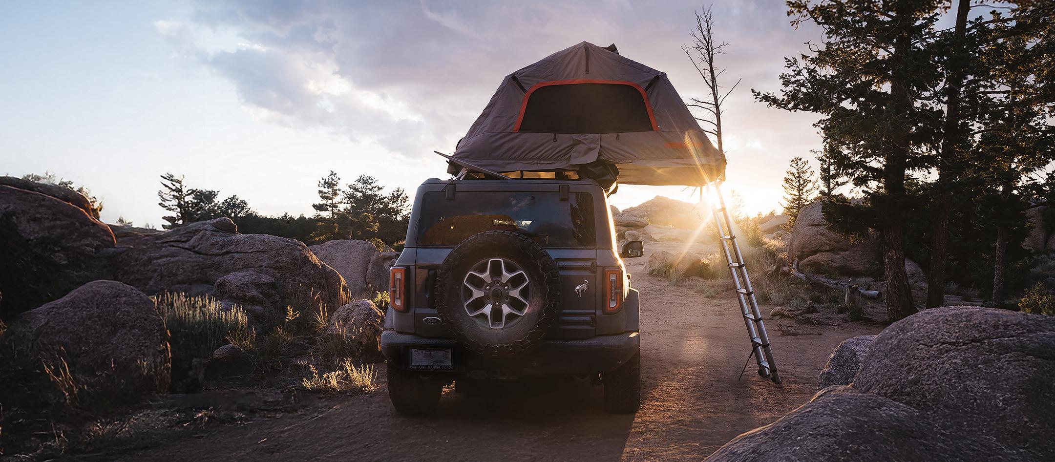 A 2026 Ford Bronco® SUV with an available accessory tent installed and open, parked on a trail at sunset