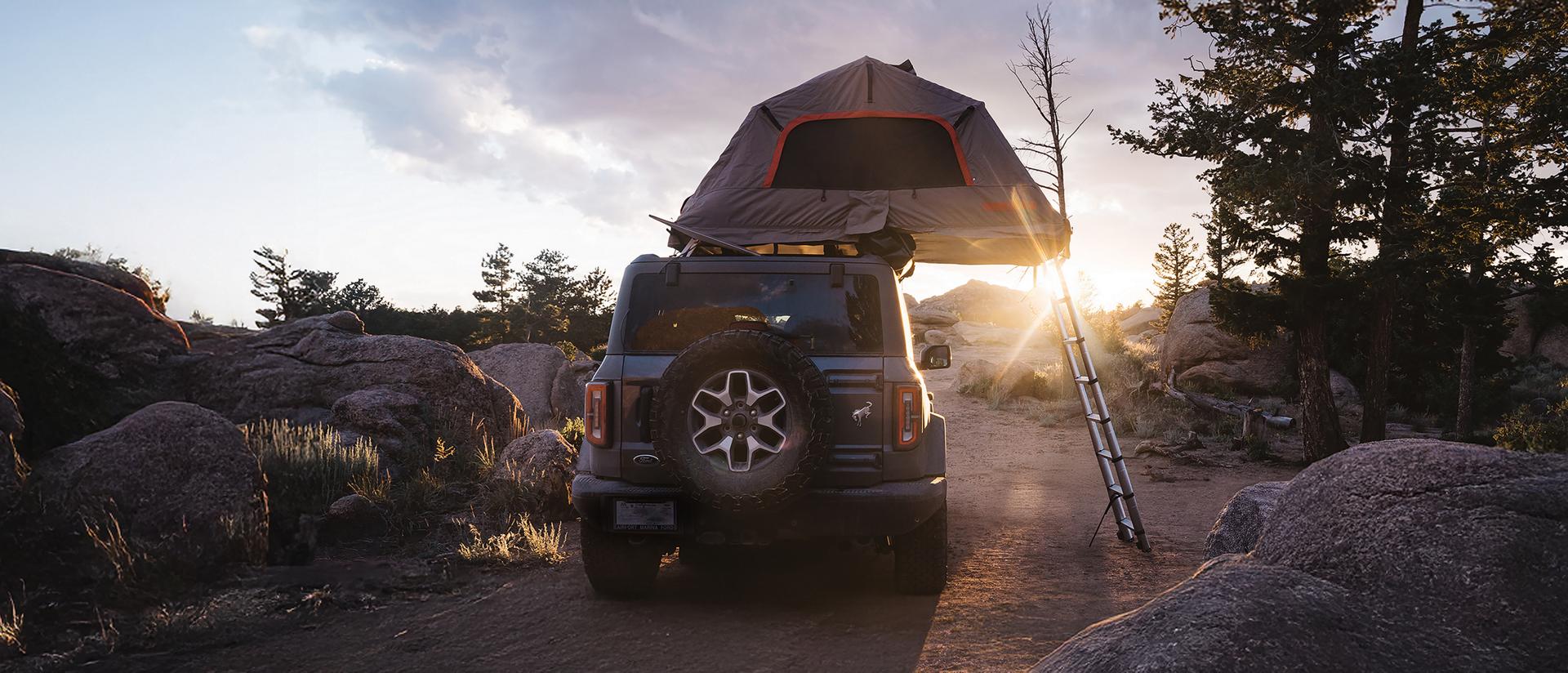 A 2026 Ford Bronco® SUV with an available accessory tent installed and open, parked on a trail at sunset