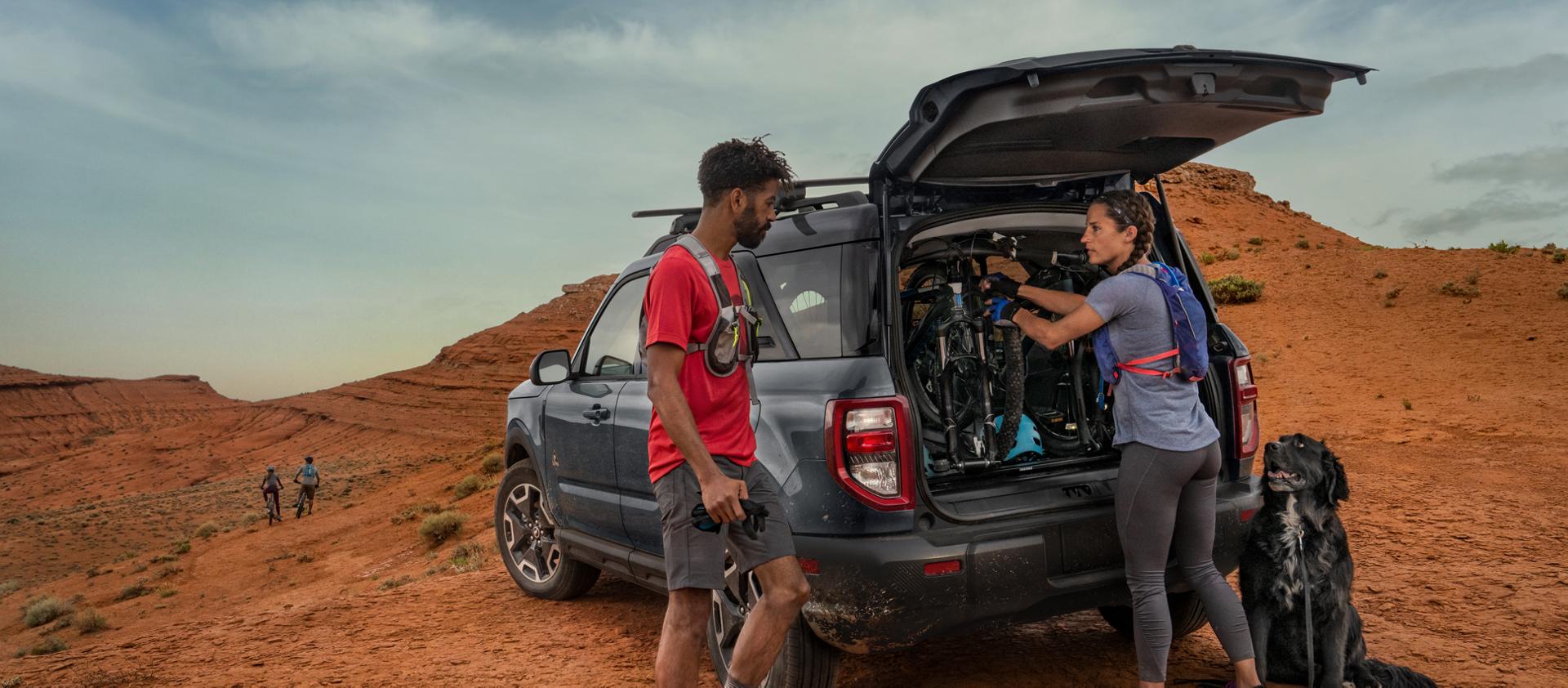 2026 Ford Bronco Sport® parked in the desert with two people standing outside of the vehicle, wearing hiking gear with their dog